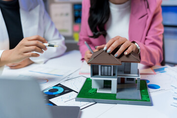 Businesswomen analyzing property market data and house model, discussing investment strategies and home buying decisions