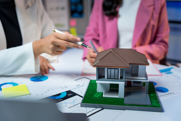 Businesswomen analyzing financial charts and a house model, discussing property investment and mortgage planning