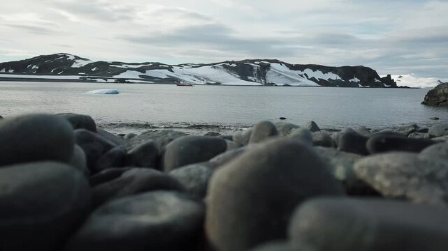 Aerial Antarctica ocean bay coastline winter landscape. Snow-covered rocky island under bright sun blue sky. Untouched wilderness of Arctic nature, mountain in background. Explore travel to South Pole