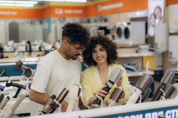 Couple Exploring Hair Styling Tools in an Electronics Store Setting. Couple buys a curling iron, hair dryer, hair straightener