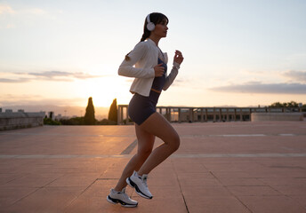 Young woman jogging with headphones during sunset in city
