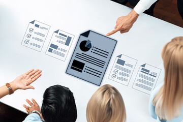 A diverse team engages in a productive discussion over project reports and data visuals, fostering collaboration and strategic planning in a modern office environment. Trope