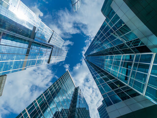 Glass towers rise around viewer forming futuristic cityscape under bright blue sky