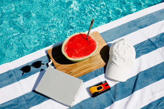 Watermelon with a spoon, sunglasses, a hat, a camera, and a book