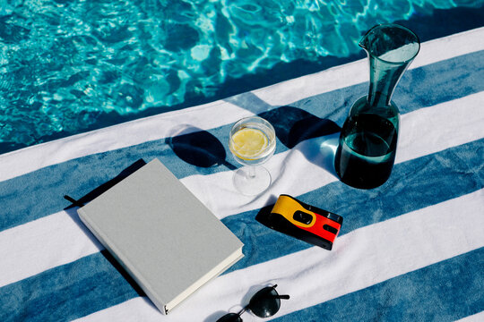 Still life showing summer objects next to a pool on a striped towel
