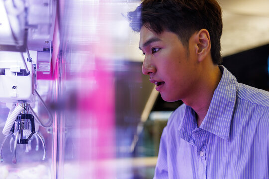 Man intently watches claw machine, hoping for a prize.