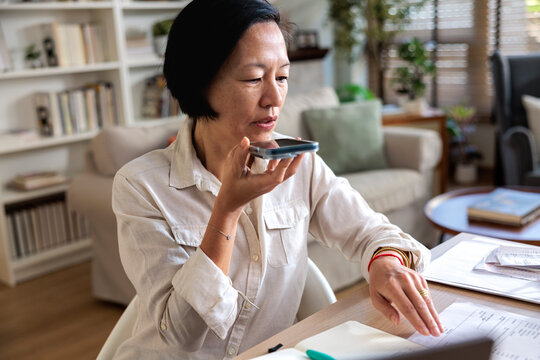 Woman dictating into phone while reviewing documents at desk.