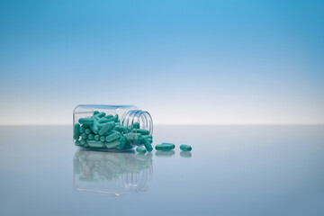 Teal capsules spill from a clear bottle, showcasing medication