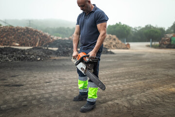 Lumberjack carrying chainsaw in wood factory