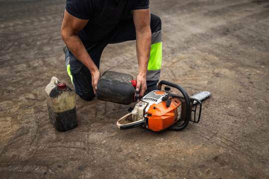 Lumberjack refueling chainsaw in wood factory