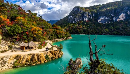 Autumnal lake nestled in a mountain valley.  Colorful foliage hugs the shoreline, with a secluded hut on a sandy bank.  Turquoise water reflects the sky