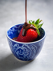 A Decadent Delight: Sweet Strawberry Covered in Silky Melted Chocolate Drizzle Nestled in a Charming Blue Patterned Bowl