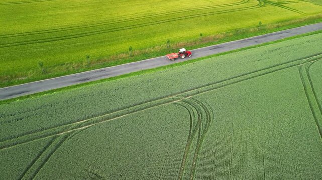 Red tractor with trailer driving on the road between fields