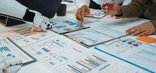 A diverse group of professionals collaborates in a modern office setting, utilizing robotic assistance for effective data analysis and presentations on various reports.Noogenesis