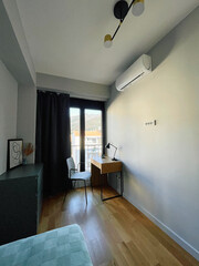 A Contemporary Bedroom Setting Featuring Modern Decor Elements, A Stylish Desk, Comfortable Chair, Large Windows, And Functional Air Conditioning Unit