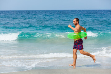 Happy bearded hipster in inflatable ring have fun on beach walk. Funny man run along sea surf and jump by water pool. Family travel lifestyle, swimming activities. Summer vacation on tropical island.