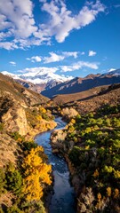 High-angle view of a winding river flowing through a valley, framed by colorful autumn foliage and snow-capped mountains