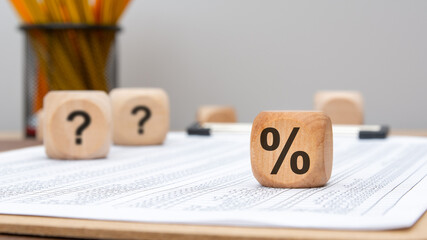 wooden cube with percent sign and question marks on financial document in office