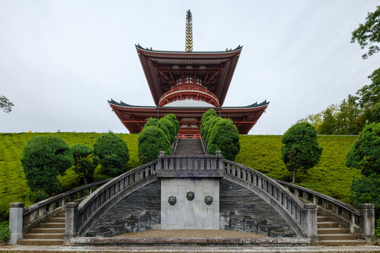 View of a majestic, multi-tiered pagoda rises above manicured green hills and a symmetrical stone staircase, a blend of architectural grandeur and nature's artistry, Narita, Chiba, Japan.