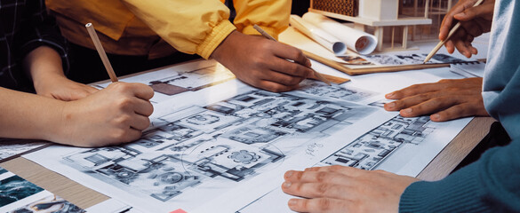 A lively scene showcasing several hands actively collaborating on intricate architectural floor plans and sketches, highlighting teamwork and the creative process in design. SACTR