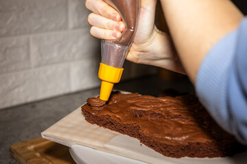 Woman decorates a chocolate cake with a pastry bag. Prepare a cake for commercial bakery.