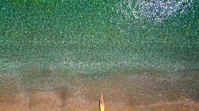 Woman in yellow swimsuit lays on a sandy beach, top down view