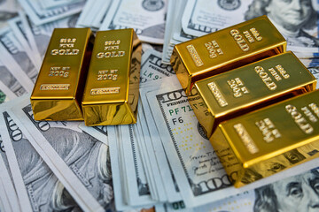 Shiny gold bullion bars on hundred dollar banknotes representing luxury, savings and financial...