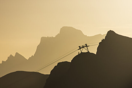 View of jagged peaks fading into the hazy horizon, cable car lines slicing through the air in the Dolomites, Pordoi Pass, Trentino-South Tyrol, Italy.