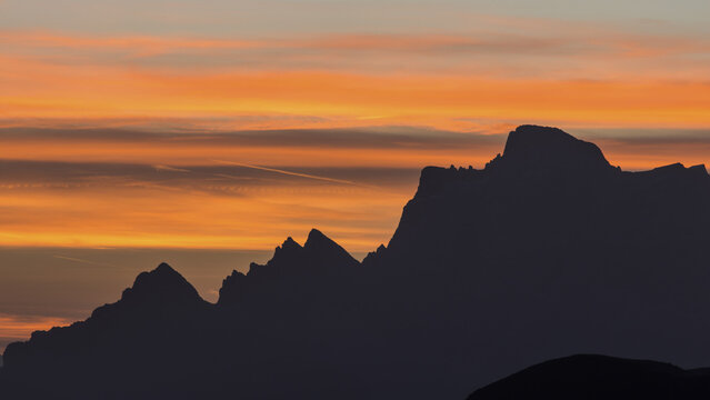 View of jagged mountain peaks silhouetted against a vibrant sunset sky painted with fiery oranges and soft yellows, Pordoi Pass, Trentino-South Tyrol, Italy.