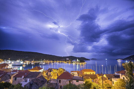 View of dramatic lightning rips through the night sky above the calm waters reflecting city lights, illuminating the town, Vis, Split-Dalmatia County, Croatia.
