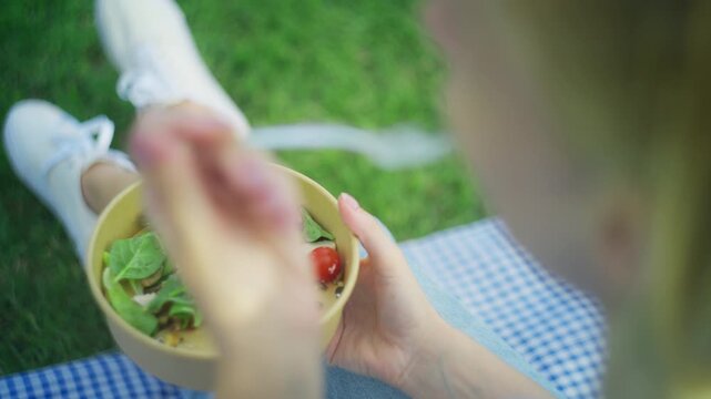 Young woman sitting on gingham blanket in park, enjoy healthy and nutritious vegetable salad from bowl for lunch, promoting balanced diet and wellness lifestyle