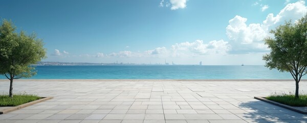 Empty waterfront park with stone floor overlooks calm blue sea. Trees line the paved area under a bright sky with fluffy white clouds. City skyline visible in distance across water.