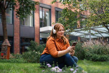 Confident woman relaxing, listening podcast outdoors in park.