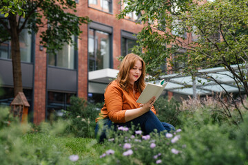 Confident woman relaxing, reading book outdoors in park.