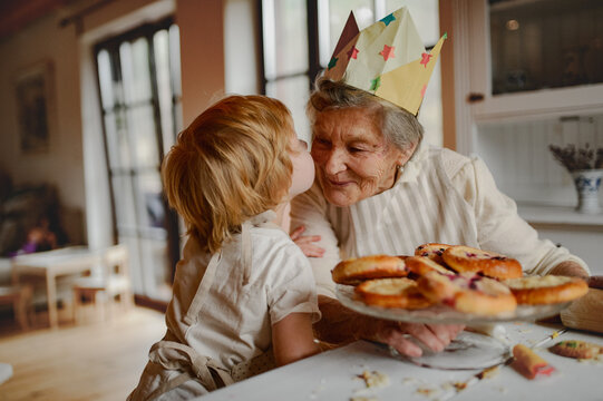 Grandmother in paper crown receiving kiss from grandchild.