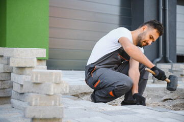 Worker skillfully laying paving stones using a hammer and wearing gloves, showcasing precision