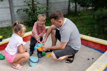 Father enjoys quality time with his children in the sandbox at a local park on a sunny afternoon