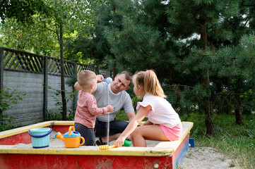Father enjoys quality time with his children in a sandbox on a sunny day in the garden
