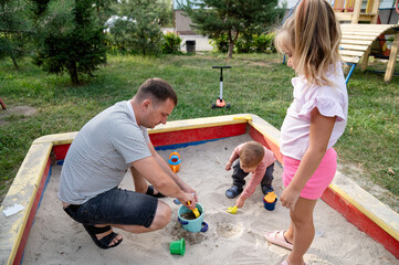Father enjoys quality time with kids in a sandbox on a sunny day at the park
