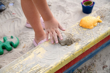 Children playing in the sandbox. A child's hand corrects a sand figure made with a mold