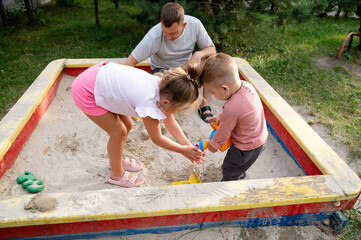 Children are playing in the sandbox. They pour water from a watering can onto each other's hands in a sunny park