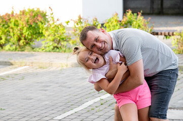 Father enjoys playtime with daughter in a sunny outdoor setting during afternoon stroll