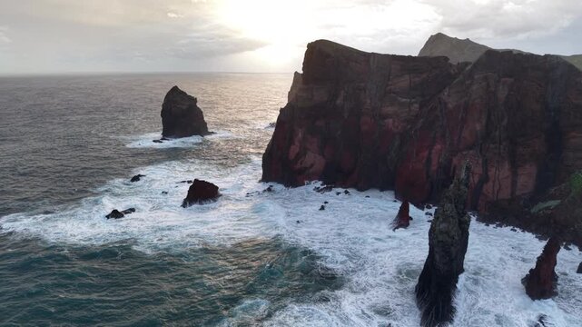 Aerial view of the rugged coastline, waves crashing against the rocks, creating a dynamic scene of dark cliffs and foamy water, Canical, Madeira, Portugal.
