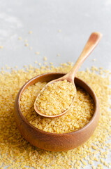 Golden bulgur wheat grains in a wooden bowl with a wooden spoon, surrounded by scattered grains, showcasing healthy grains and natural food presentation