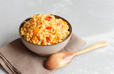 Bowl of cooked bulgur wheat with vegetables, yellow and red peppers, served on a brown napkin, showcasing a healthy and vibrant meal option for nutritious eating