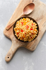 Colorful bowl of cooked bulgur wheat mixed with diced vegetables, placed on a wooden cutting board with a wooden spoon, showcasing a healthy and vibrant meal option