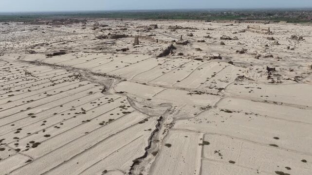 Aerial view of ancient Gaochang's textured ruins with muted sand and brown tones, and sparse greenery creating a desolate yet intriguing landscape, Gaochang, China.