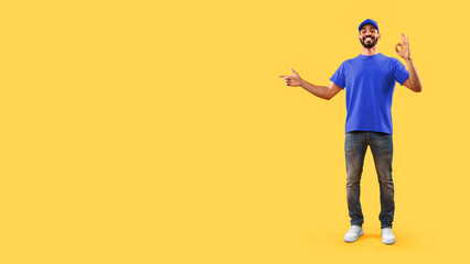 Look There. Arabic Male Delivery Worker Gesturing Okay Showing Free Space For Text Standing Over Yellow Studio Background. Guy Advertising Courier Service Concept. Panorama