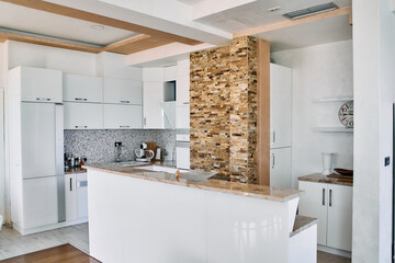 Modern Kitchen Design Showcasing Sleek White Cabinets, Elegant Stone Wall, and Contemporary Appliances for an Inviting Culinary Space