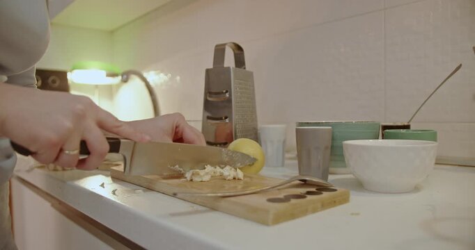 A woman is meticulously chopping garlic on a wooden cutting board in preparation for a delicious and flavorful meal.